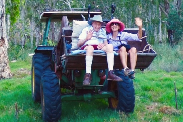 David Goodall and a woman sit in the bucket of a tractor on a station in the Kimberley.