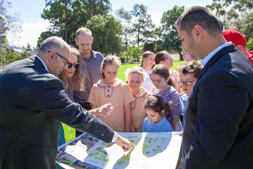 Mayor Kahl Asfour shows off a map of the new playground to a group of people