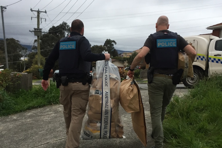 Two police officers walking away holding two large plastic bags 