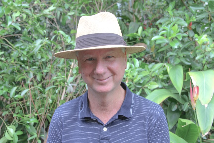 A man in a hat stands in a garden
