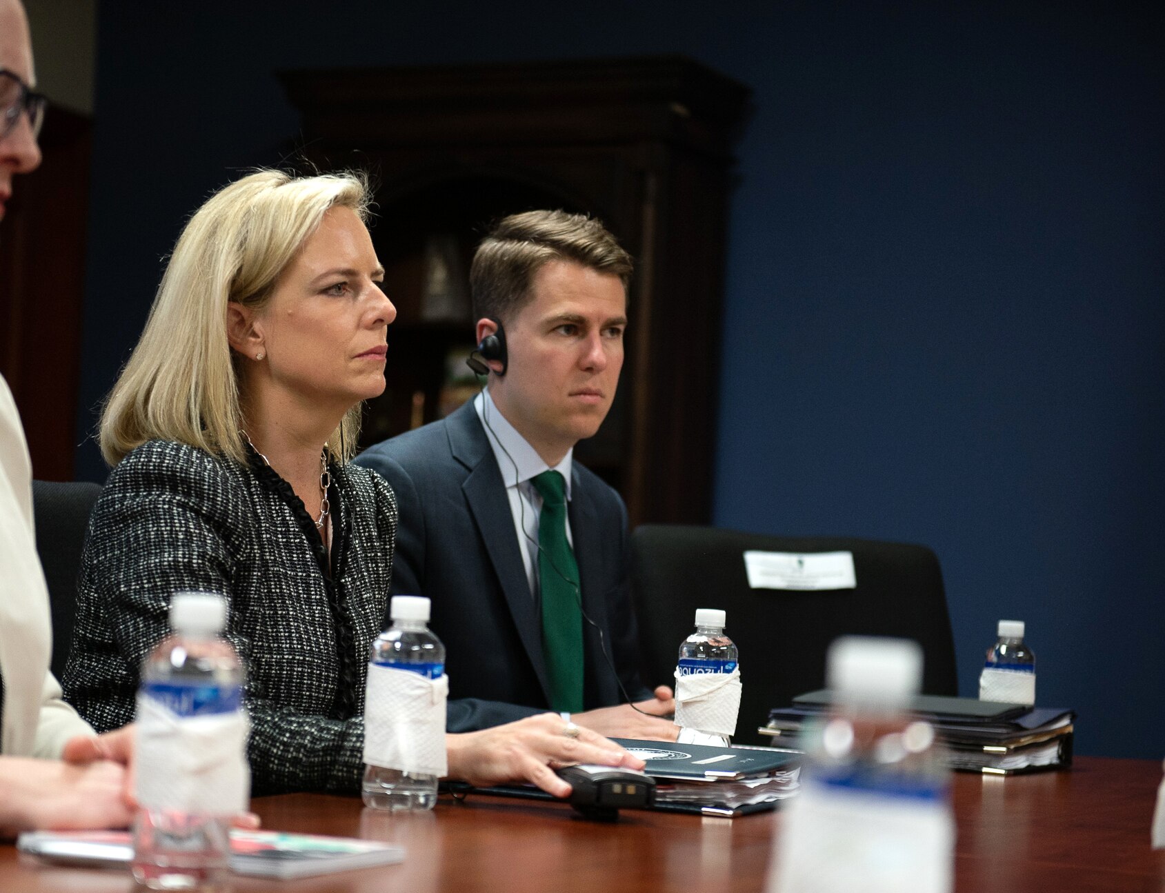 Miles Taylor sits next to a woman at a table. He has an earpiece on.