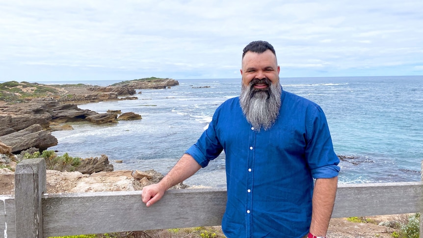 A man standing and smiling in front of an ocean view.