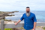 A man standing and smiling in front of an ocean view.