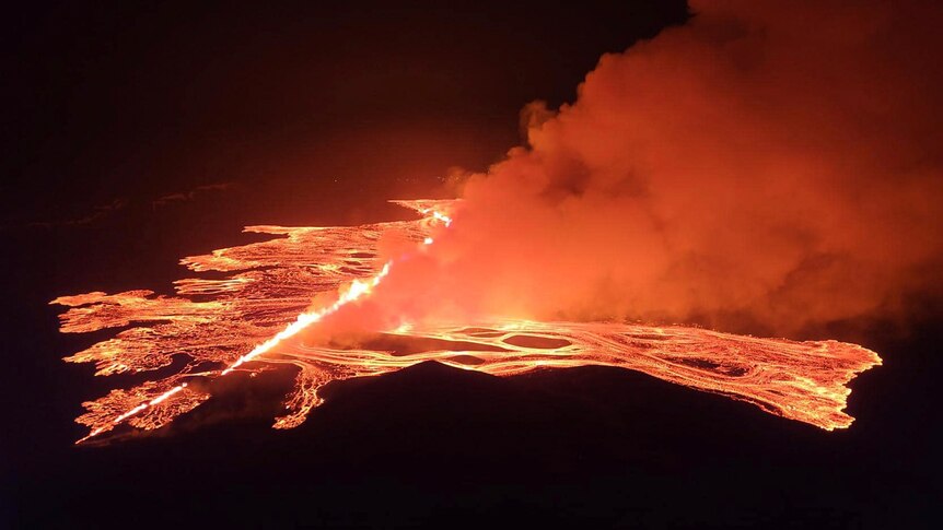 A night time photo of a row of flames and lava rise from a crack in the earth.