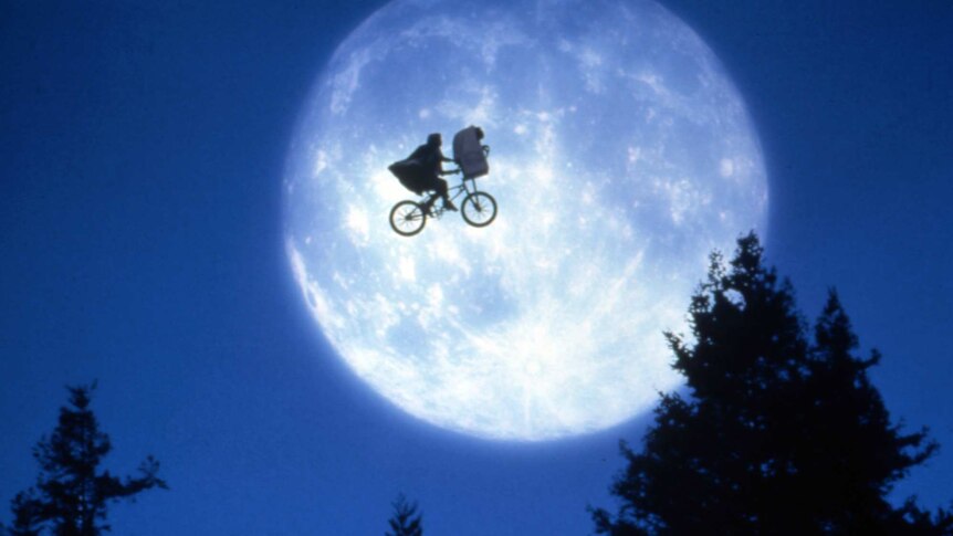 A still from the movie E.T., featuring a young boy riding a bicycle, silhouetted against the moon.