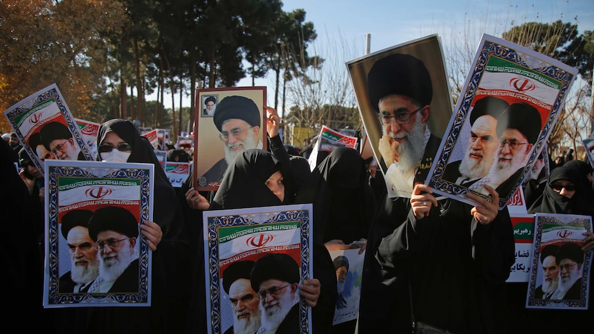 A crowd of women dressed in black hold up portraits of Iranian Supreme Leaders.