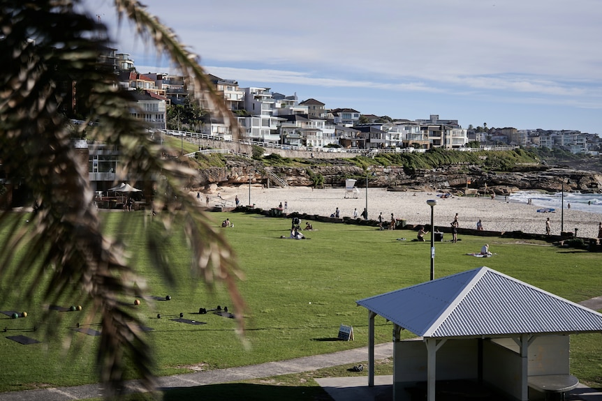 A wide angle image of Bronte Beach showing the sand and grassy park with picnic shed in foreground