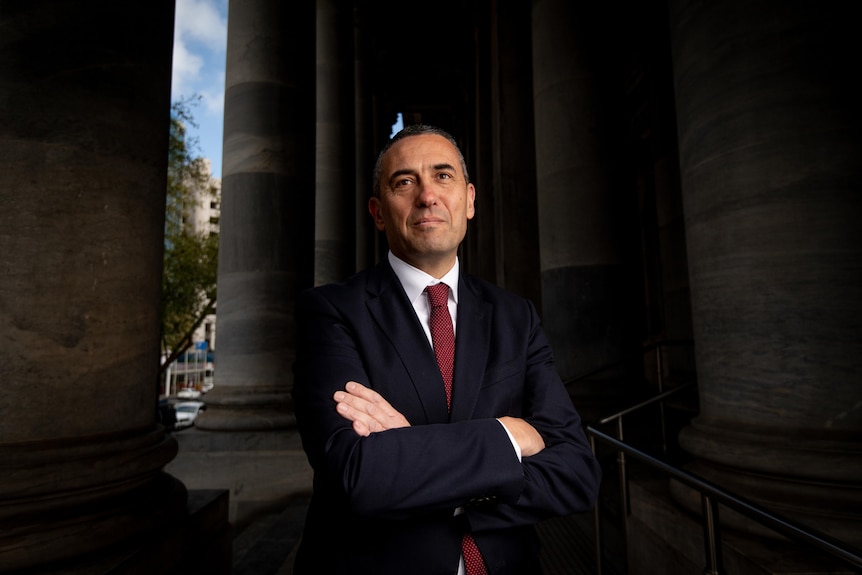 Tom Koutsantonis, a man in black suit and red tie stands on steps of parliament house with arms crossed.