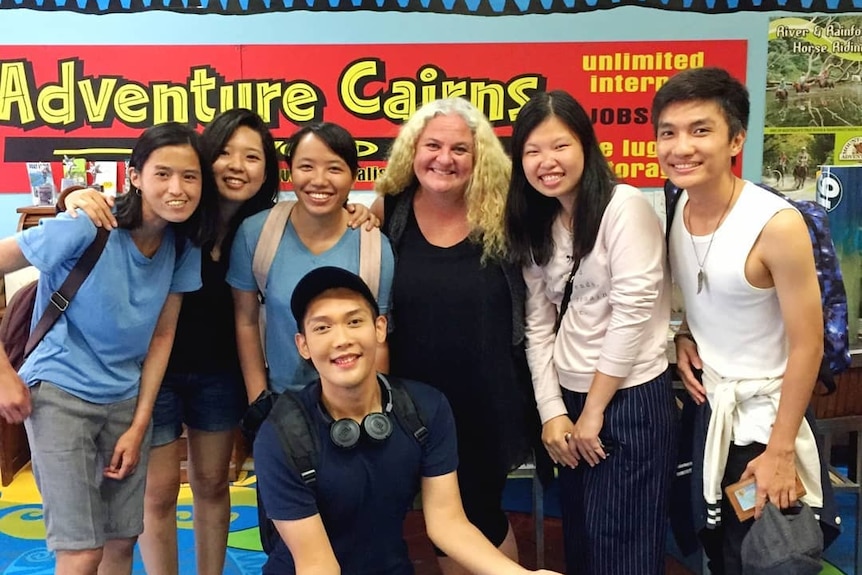 A lady with bleached hair in her shop, Adventure Cairns, smiling with a group of Indonesian backpackers.