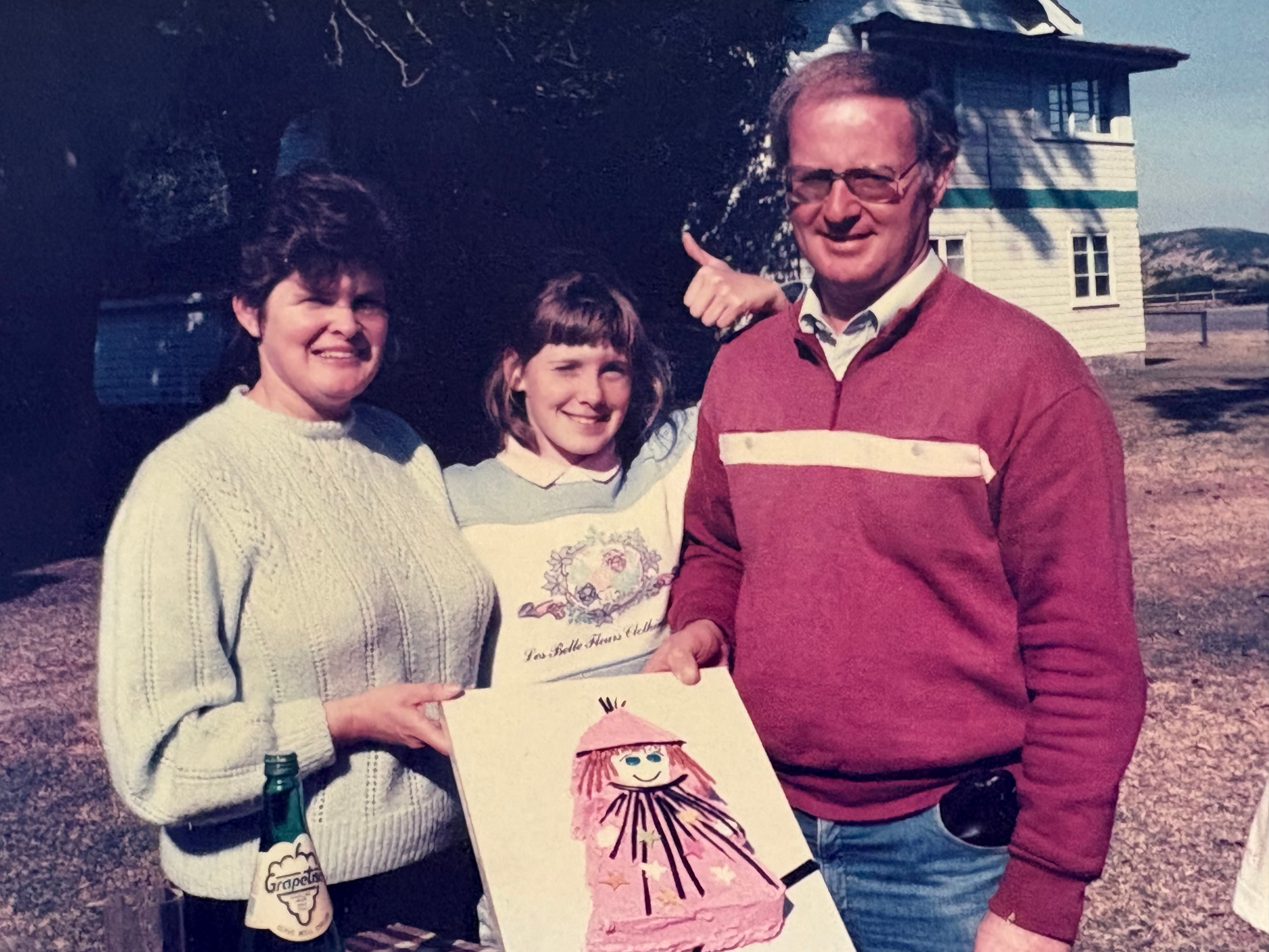 A girl in a blue and white jumper pictured with her parents holding a drawing 