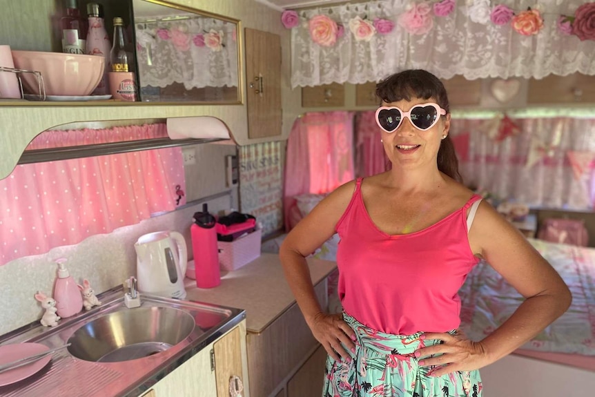 A woman with heart-shaped glasses inside her very pink vintage caravan.