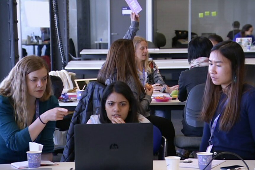 Women taking part in the SheHacks program look at a laptop.