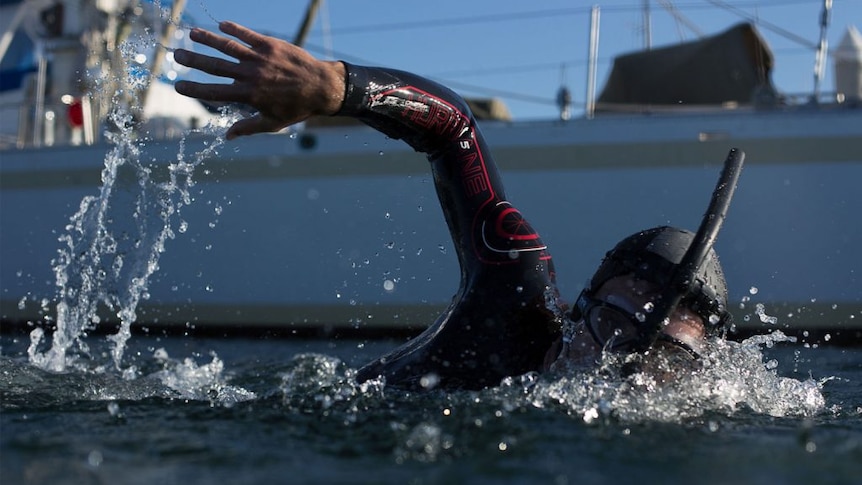 A close-up of Ben swimming in the ocean in a wetsuit with goggles and a snorkel.