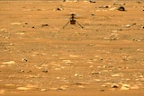 A small helicopter-like drown hovers above the surface of a dry, rocky plain. 