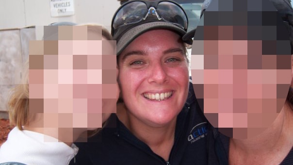 Mara Quinn smiles posing for a photo wearing a baseball cap between two other women, whose faces are pixelated.