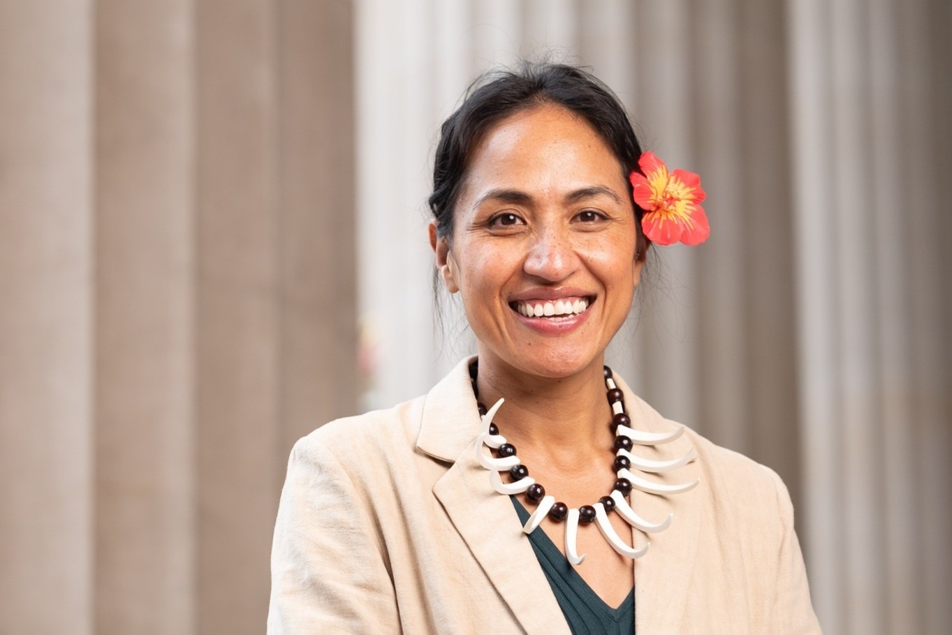 Anasina Gray-Barberio sonríe, luciendo una flor en el cabello y un tradicional collar de conchas blancas, chaqueta beige.