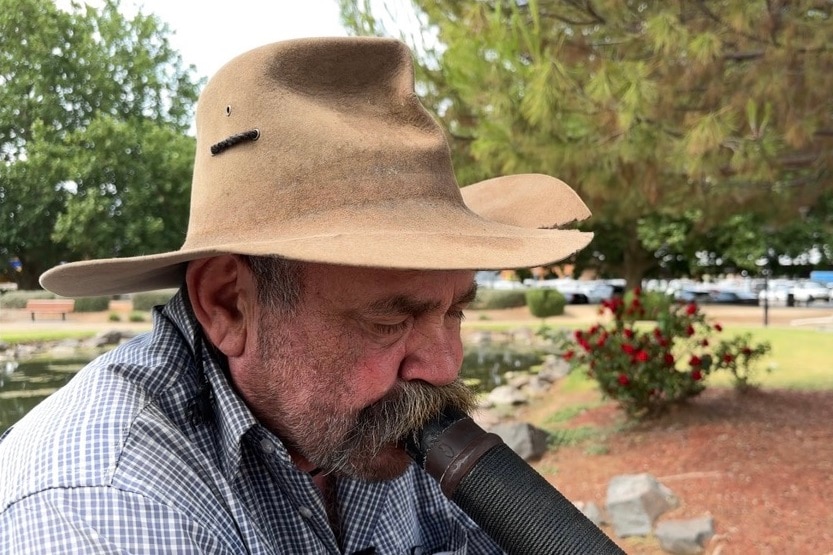 A man playing a digeridoo with a brow outback hat.