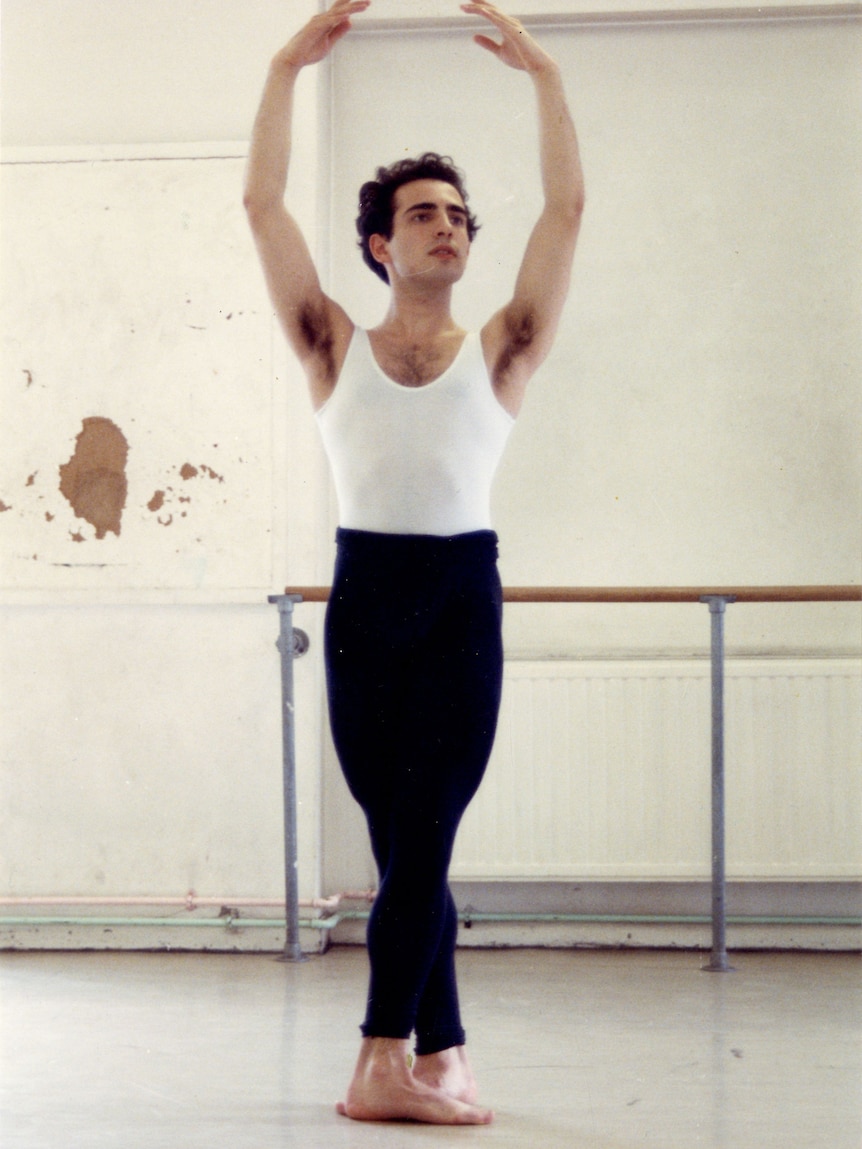 Rafael Bonachela, a young Spanish Australian man, in a dance studio, his arms raised above his head.