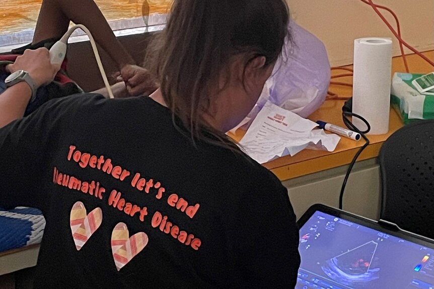 A woman wearing a black t-shirt, with her back to the camera, uses an ultrasound machine. The scan can be seen.