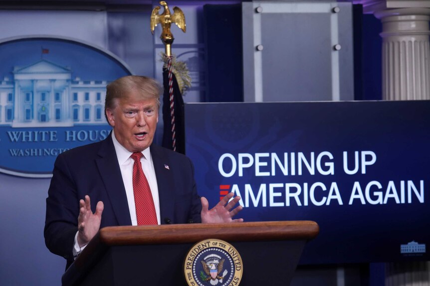 Trump gesturing next to a sign reading "Opening Up America Again"