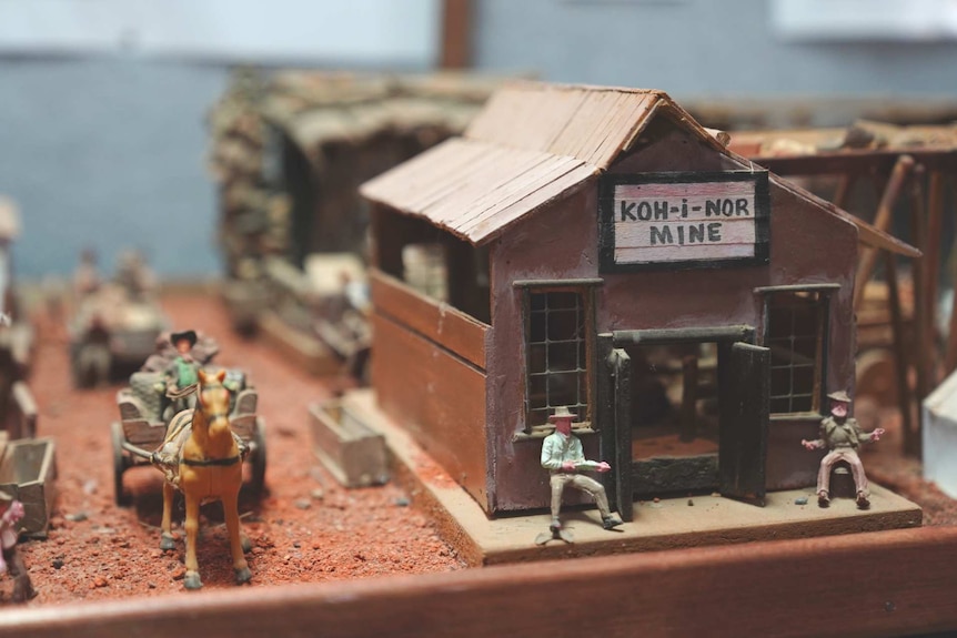 A miniature scene of a mine hut, men sitting out the front, and a man on a horse-drawn wagon.