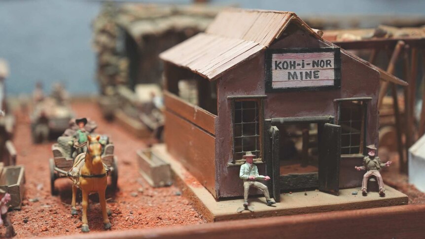 A miniature scene of a mine hut, men sitting out the front, and a man on a horse-drawn wagon.