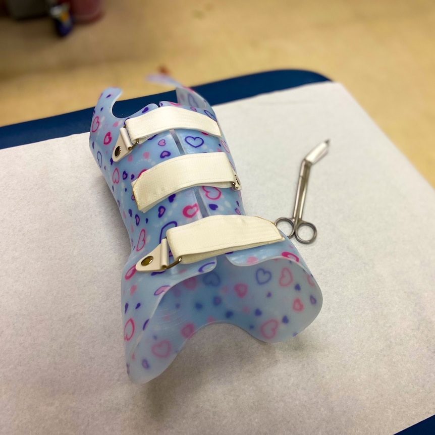 A blue plastic back brace with love hearts and velcro straps on hospital bed.