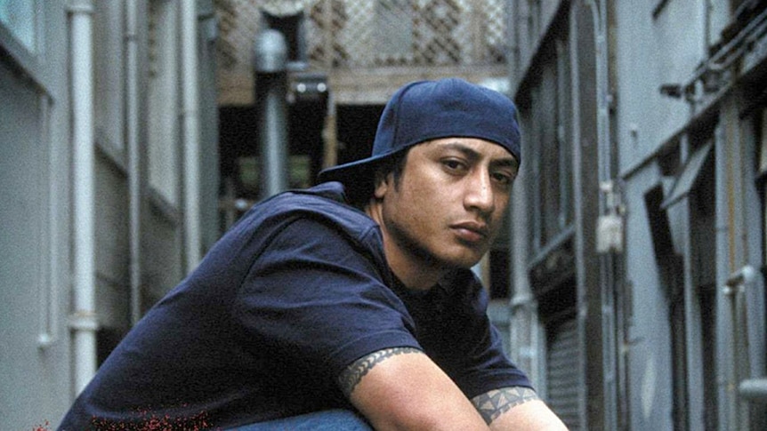 New Zealand rapper Scribe wears a blue baseball cap backwards and a blue t-shirt as he glares at the camera