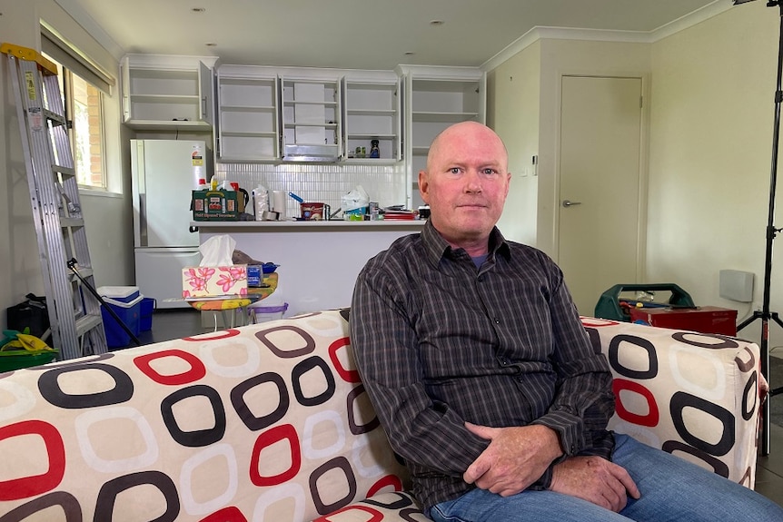 Man sitting on a couch in a unit being packed up with empty cupboards and boxes in the background.