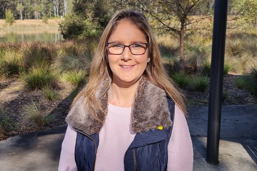 A woman wearing glasses smiles while standing outside.