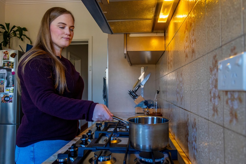 A woman holds a pot above a flame on a stove.