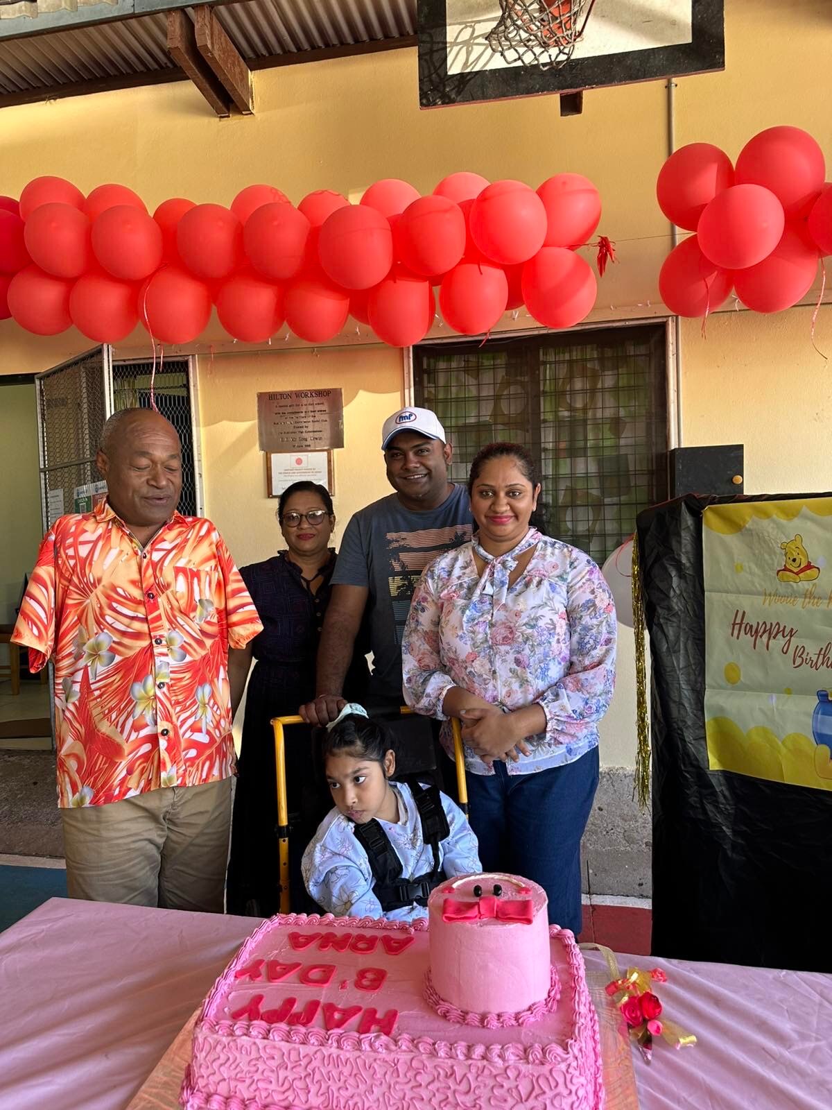 A ten-year-old girl born with a brain injury celebrates her birthday with a pink cake and her supportive family and teacher.  