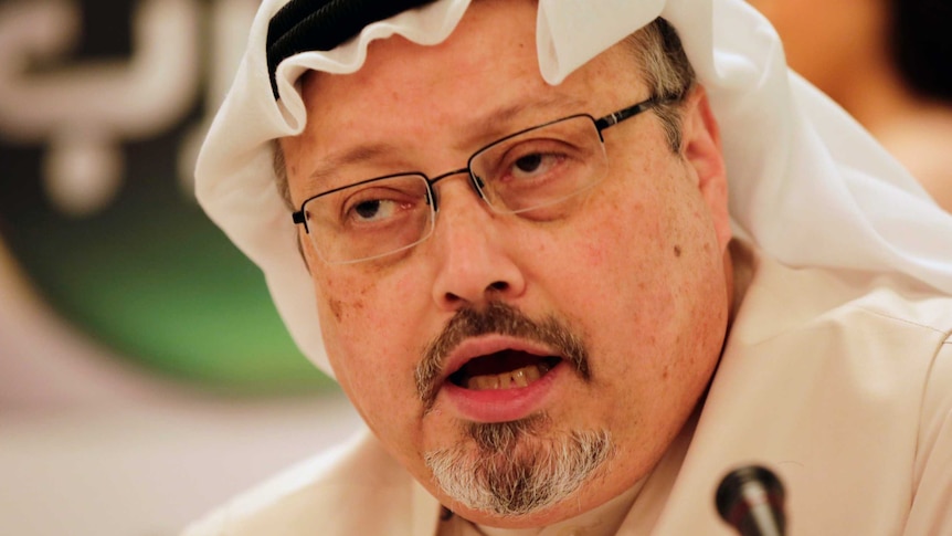 headshot of Jamal Khashoggi wearing a white head covering and glasses, mid-speech.