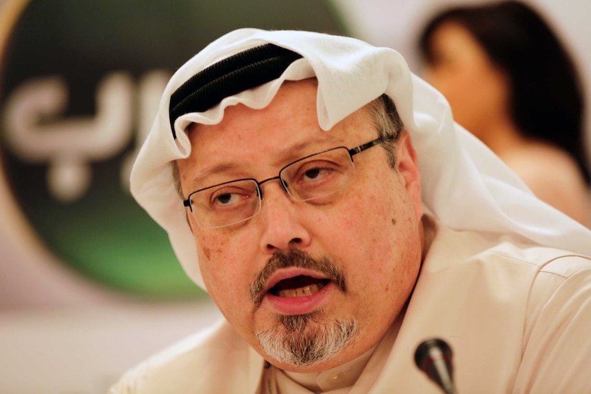 headshot of Jamal Khashoggi wearing a white head covering and glasses, mid-speech.