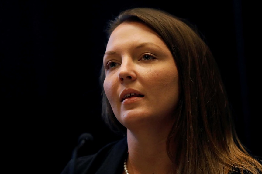 Brunette woman Courtney Wild speaks at a news conference.