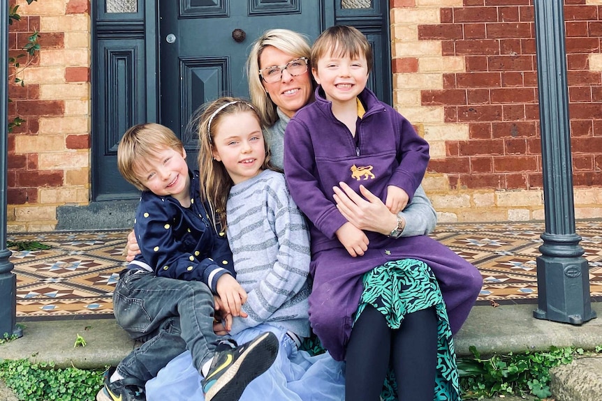 A mother sits on a doorstep with her three children sitting with her.