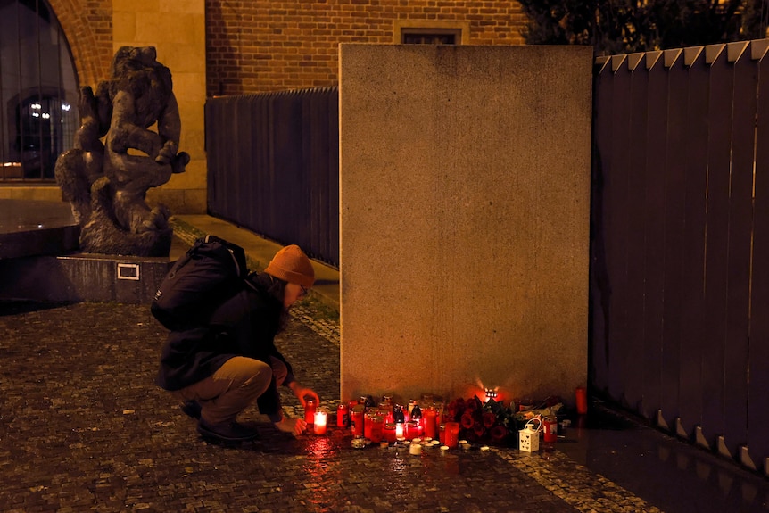 A woman lights a candle in front of Charles University main building.