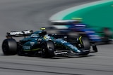 A green F1 car goes past a blue F1 car around a corner.