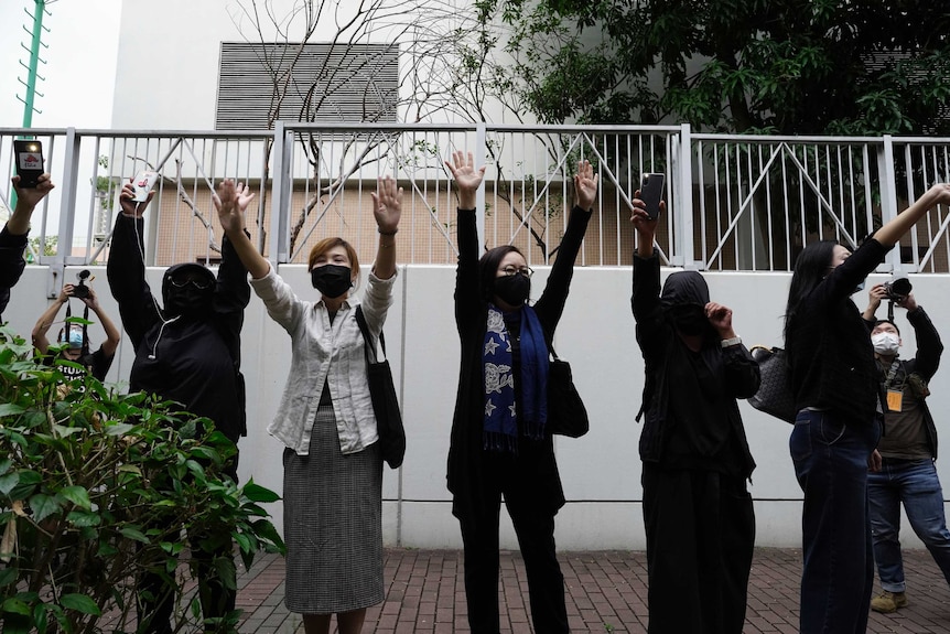 A line of people raise their hands to the camera.