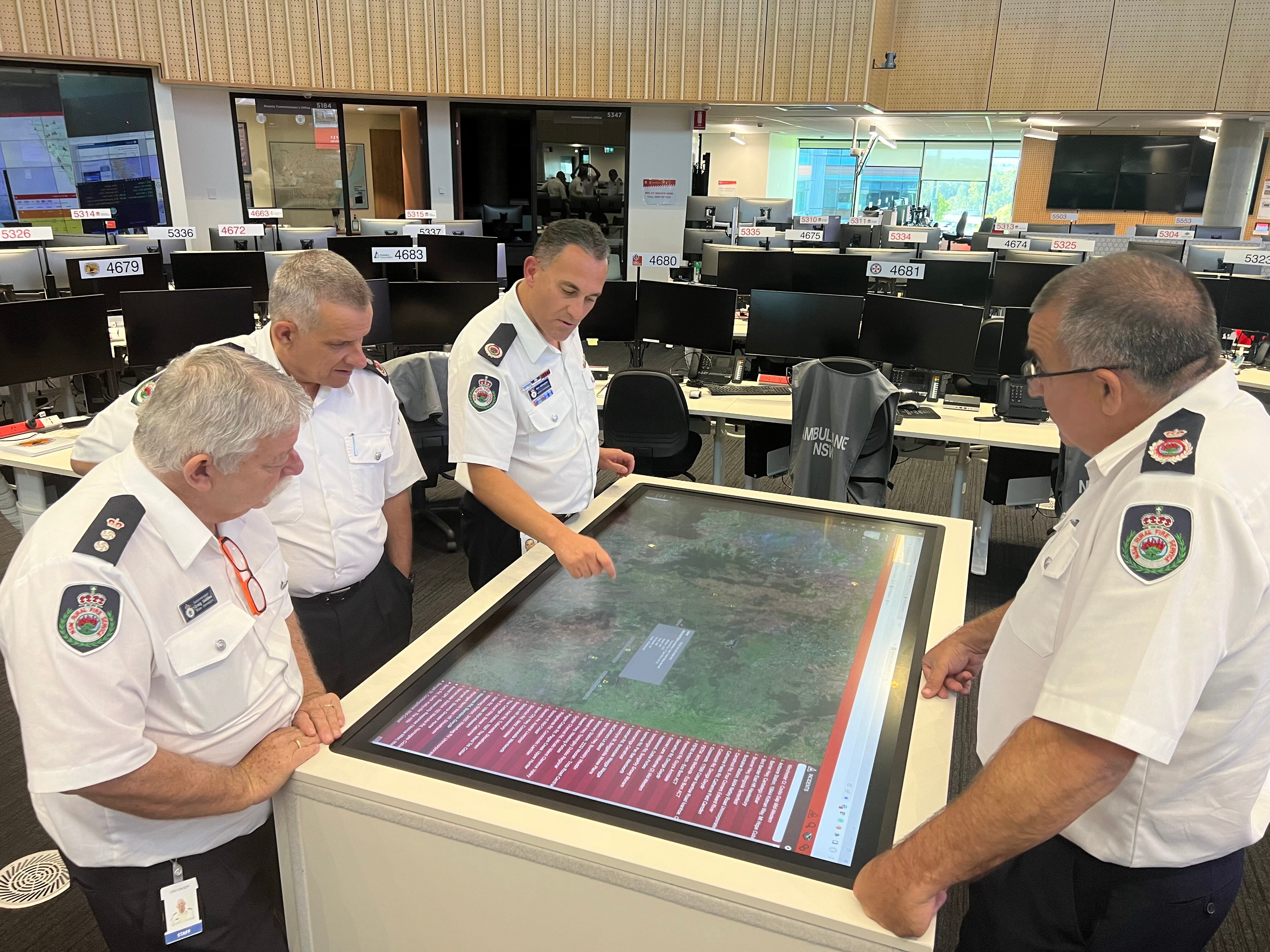 fire heads at central command look over a computer with images of terrain 