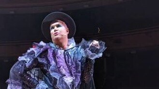 A male performer dressed in dark glitter body suit with a cape with purple ruffles