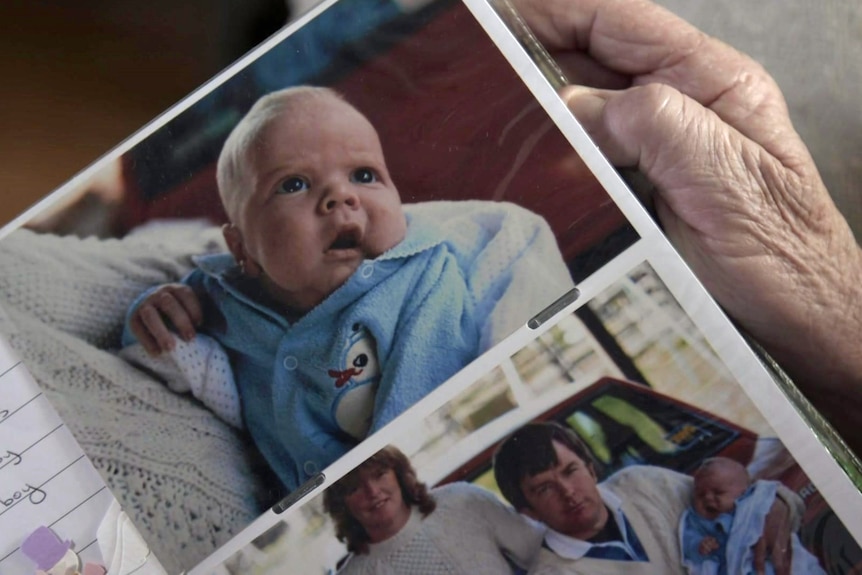 A closeup of a photo in a photo album of Peter as a baby in a blue oneie