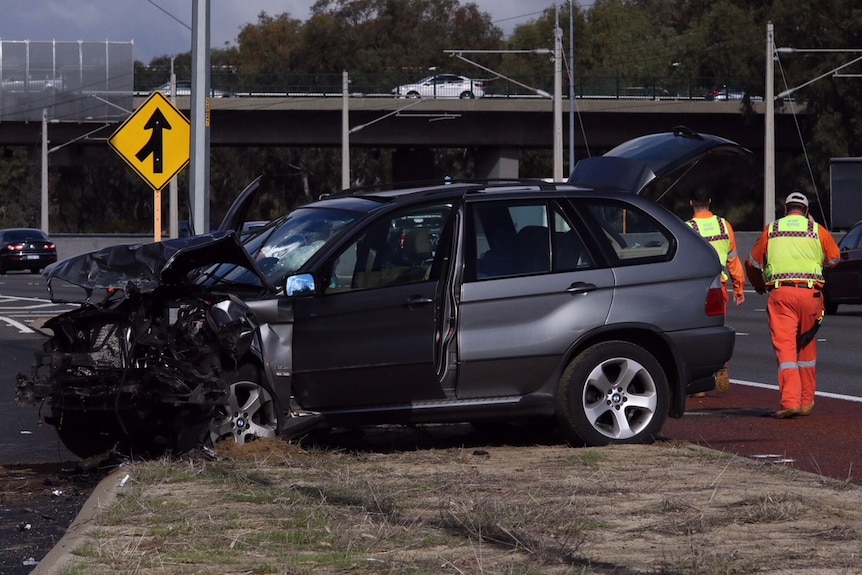 A grey BMW four-wheel-drive on the side of the freeway with a smashed front end.