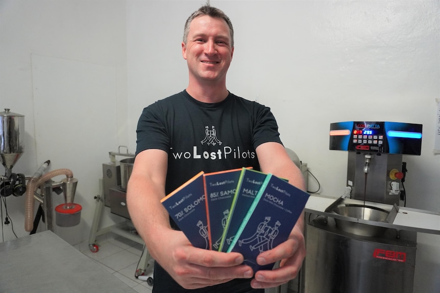 A man stands smiling holding some blocks of chocolate in cardboard boxes. 