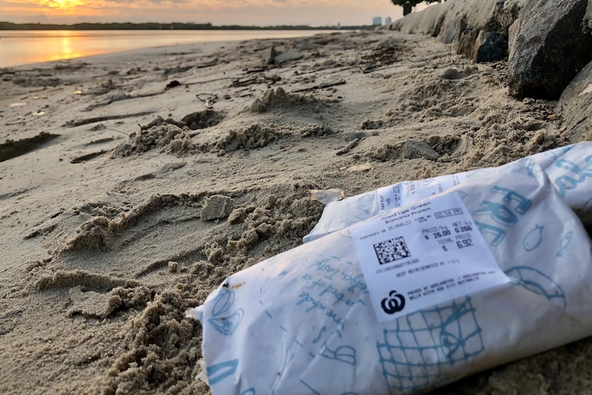 Two packets of supermarket prawns left on the sand by a river.