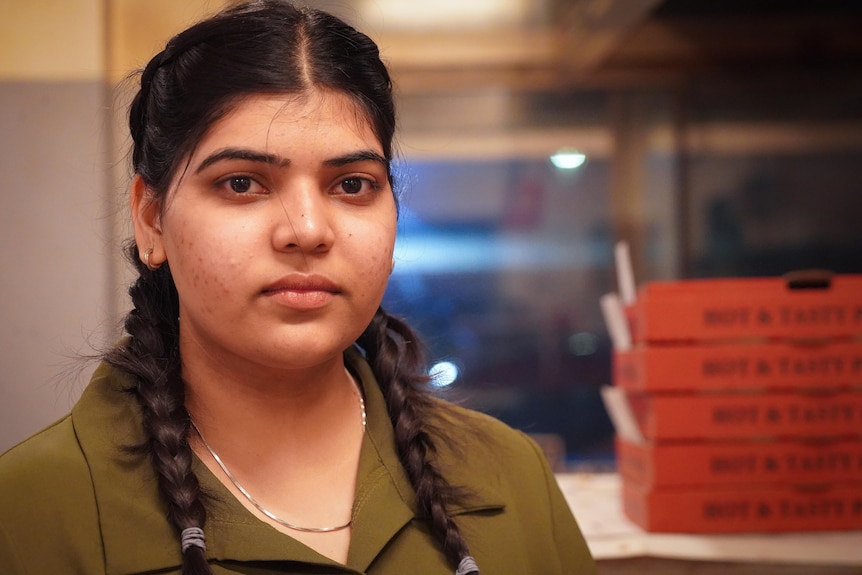 Sandeep Kaur looks at the camera with pizza boxes stacked next to her.