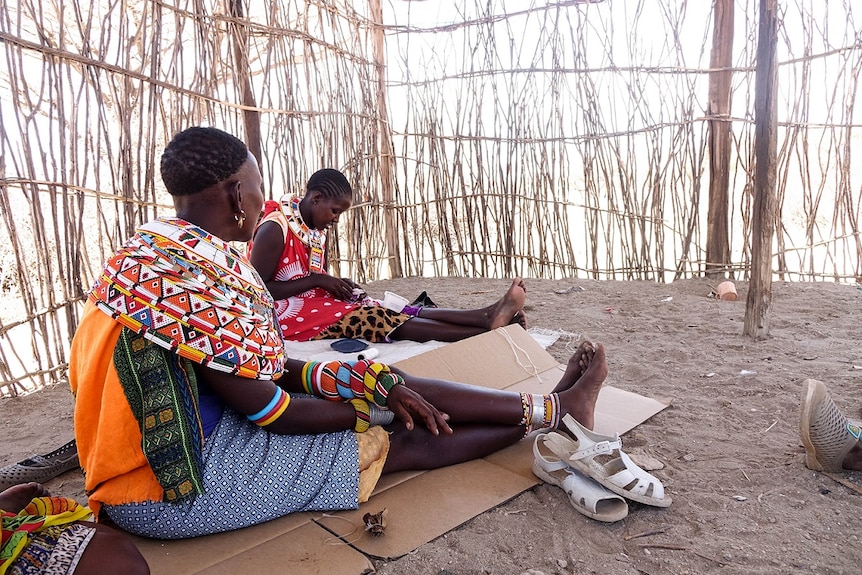Two women sit in a remote hut crafting jewellery.