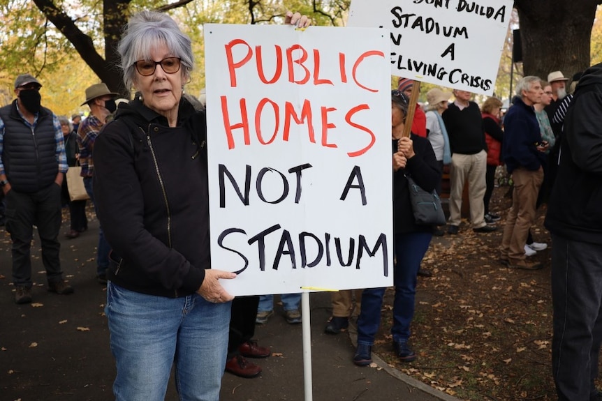 A woman holds a sign at a rally reading: Public homes not a stadium