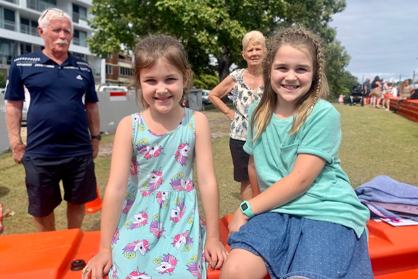 two girls sitting on border barricade, grandparents standing behind