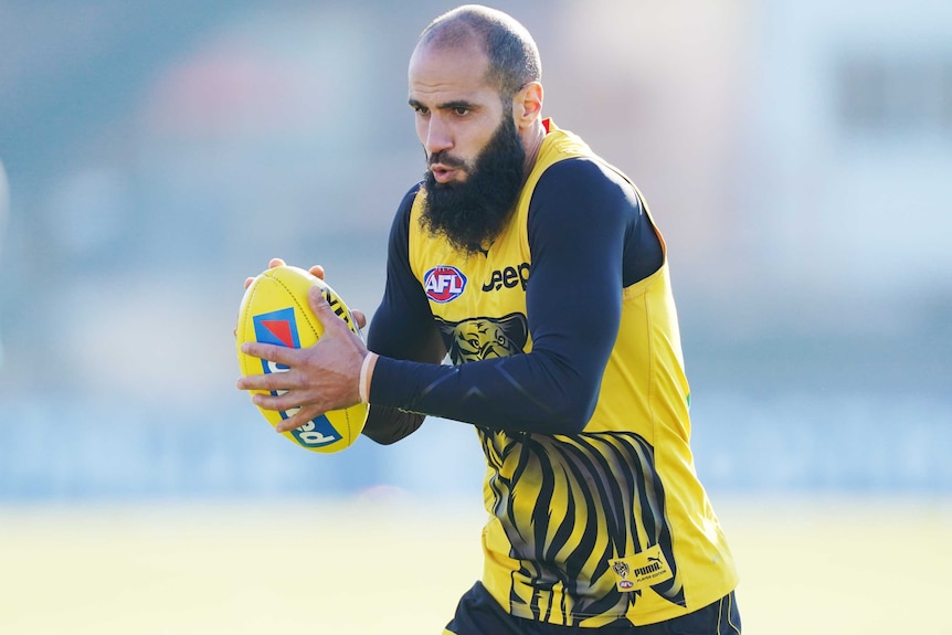 A Richmond Tigers AFL player runs with the ball held in both hands at a training session in Melbourne.